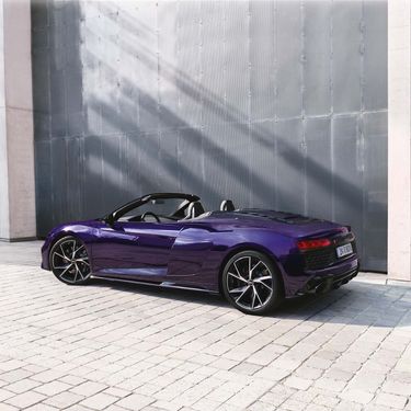 Side rear view of the R8 Coupé V10 performance RWD in purple in front of a wall of metal panels